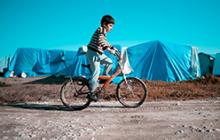 Image of Syrian boy riding a bicycle in a refugee camp 